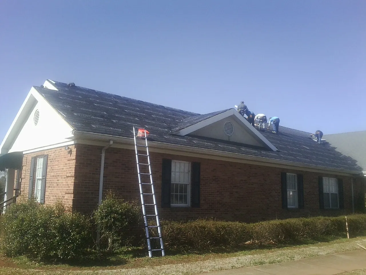 Crew tearing shingles off a brick ranch roof with a ladder set — Metal Roof Repair work by our crew in Dunlap