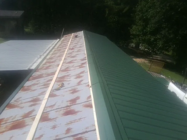 Old rusted panels beside newly installed green metal roofing — Wind Damage Roof Repair by Roofing Brothers in Dunlap
