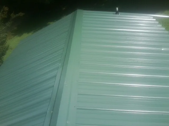 New green metal panels meeting at the ridge of a roof — Flat Roof Repair work by our crew in Dunlap