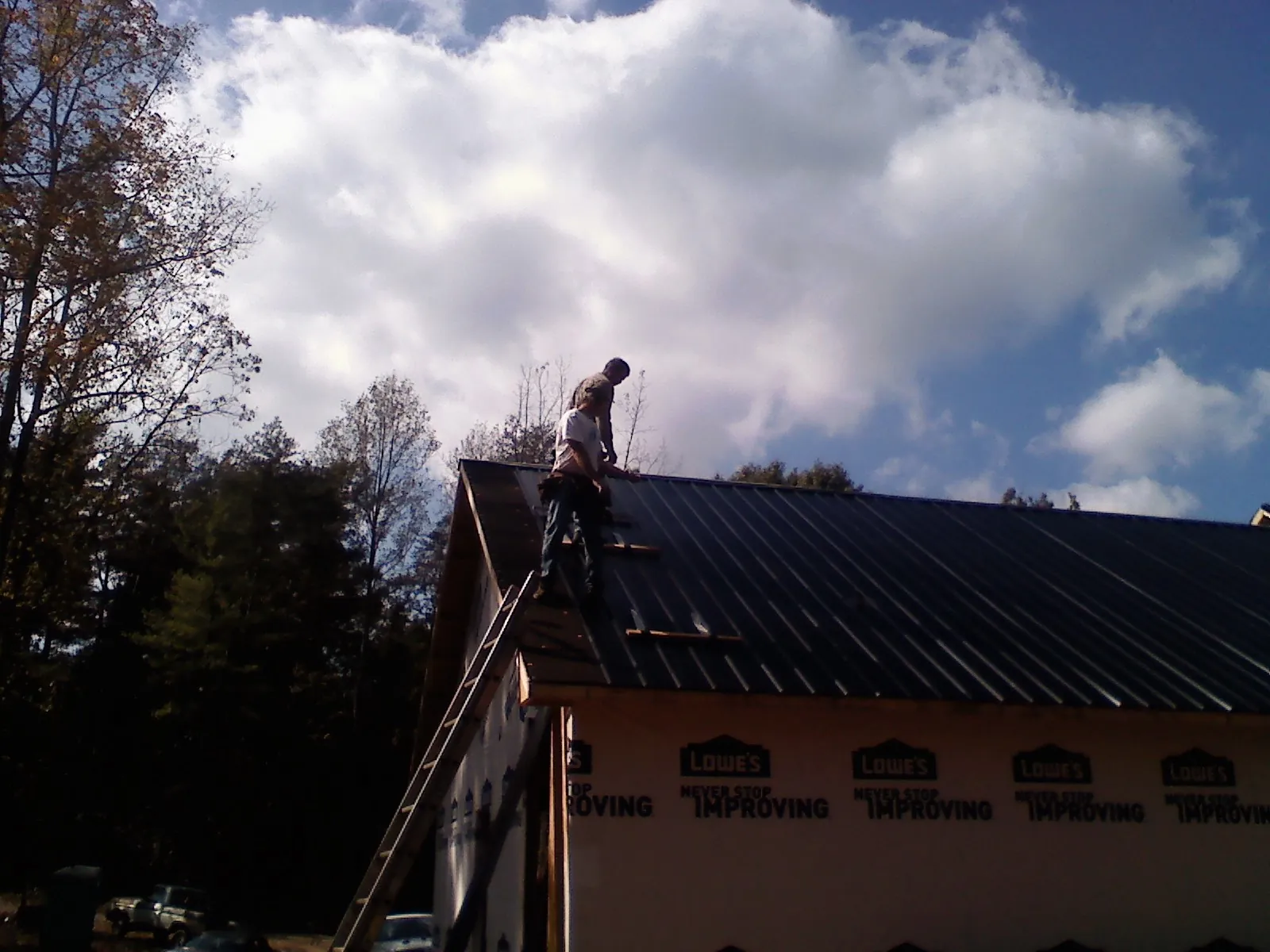 Roofer fastening dark metal panels high against a cloudy sky, from a Roof Inspection job in Dunlap