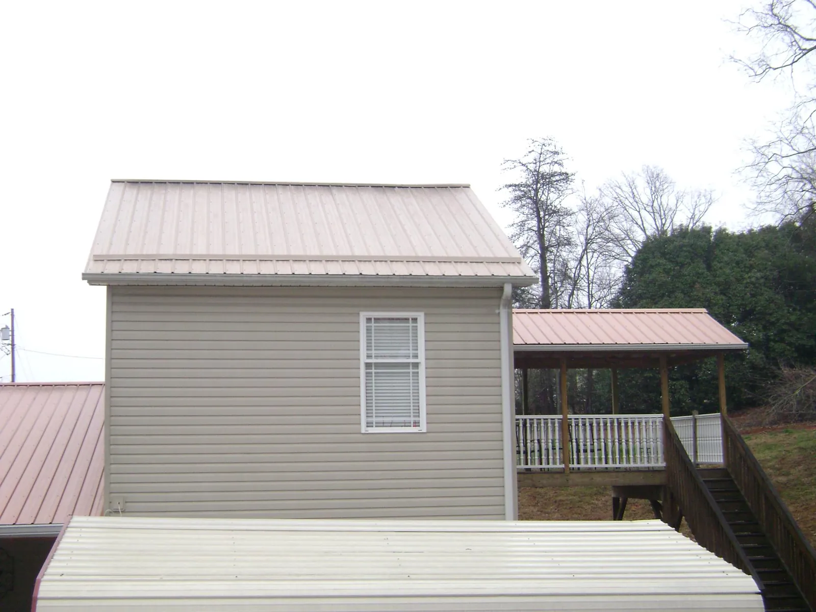 Tan metal roofs on a two story addition and attached porch, from a Roof Replacement job in Dunlap
